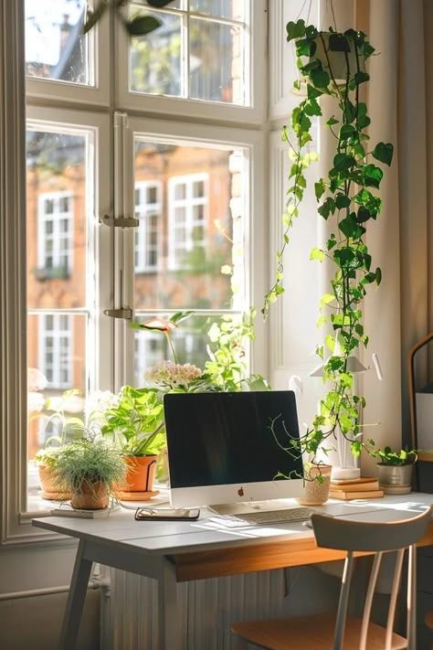 A bright home office desk positioned beside a window with a laptop, notebook and a small plant
